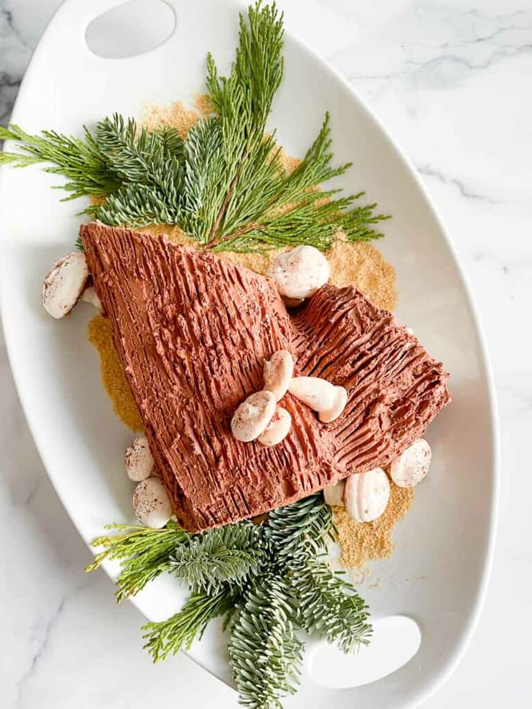 Buche de Noel cake on a platter with mushrooms and greenery.