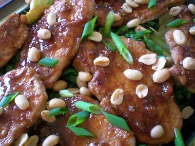 A plate of pork chops garnished with chopped green onions and whole peanuts.