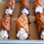 Brandy snaps, dipped in chocolate and served with espresso whipped cream, are arranged on a tray lined with parchment paper.