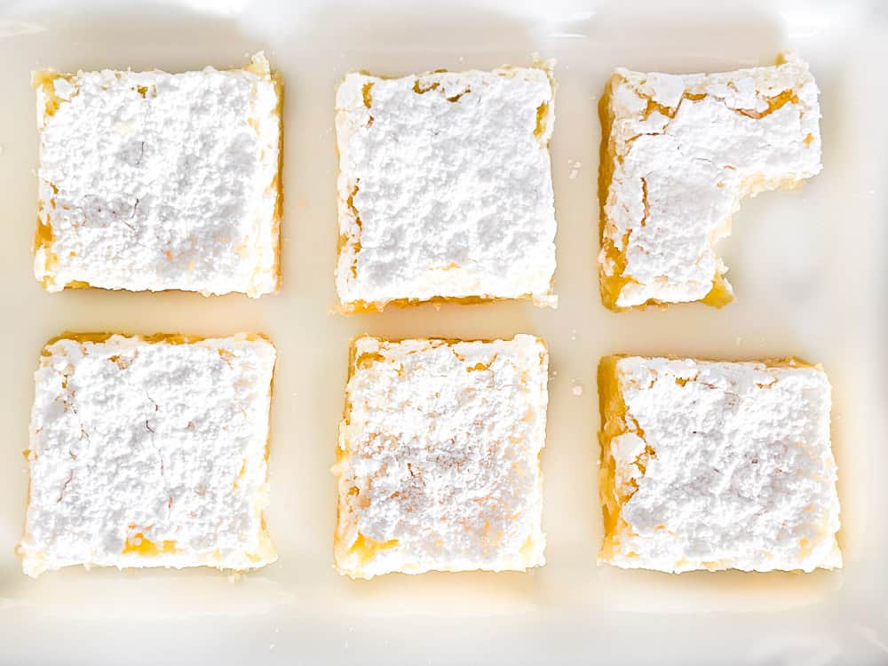 Lemon Bars on a white plate, one with a bite out of it.
