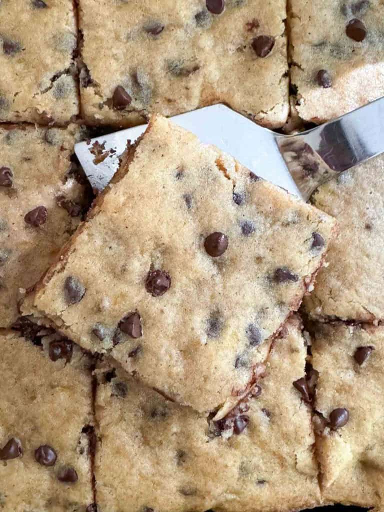 Close-up of multiple chocolate chip cookie bars, with one bar being lifted by a spatula, reminiscent of delicious banana bars.