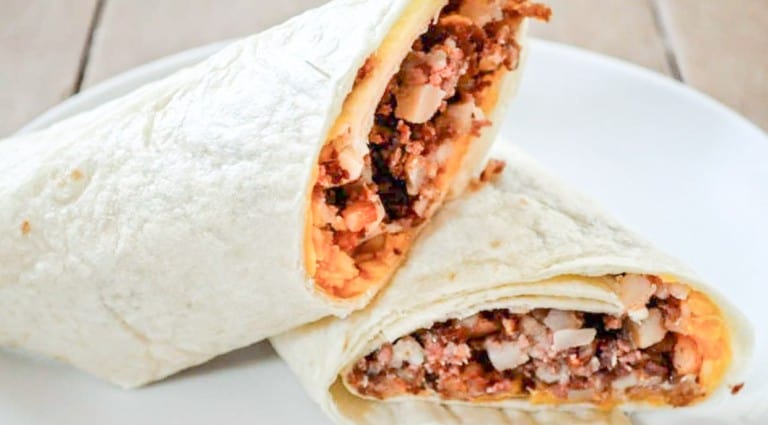 A Corned Beef Hash Breakfast Burrito with a meat and rice filling on a white plate.