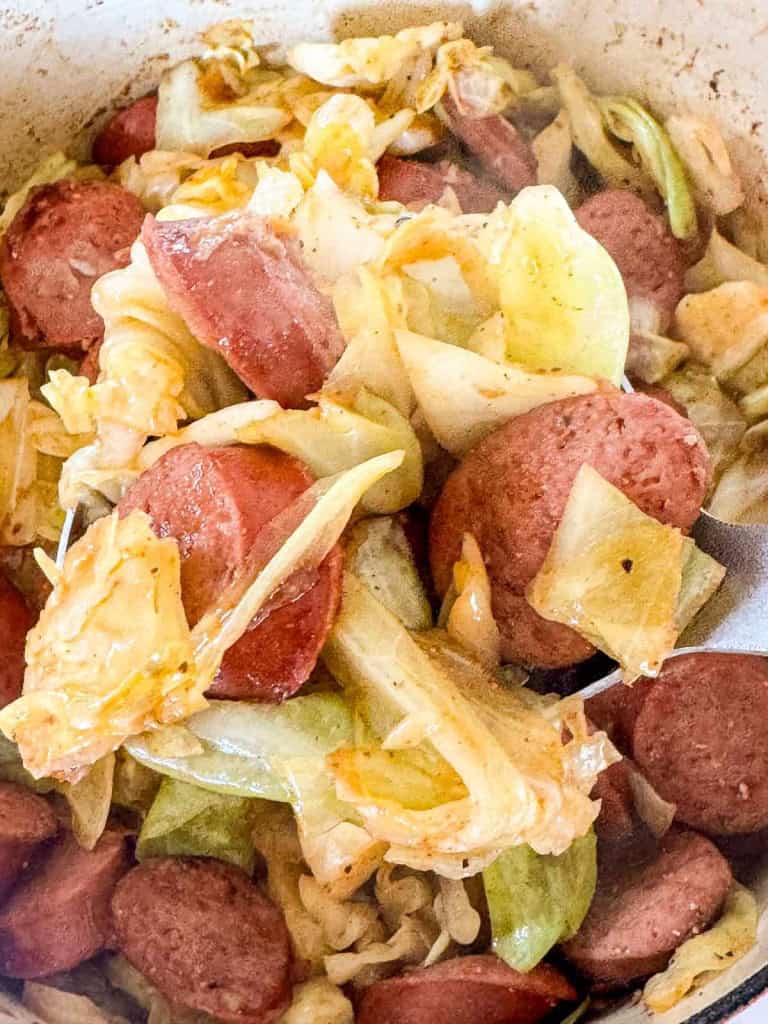 Close-up of smothered cabbage with smoked sausage. The wilted cabbage melds perfectly with the browned sausage, creating a savory blend all mixed together in a pan.