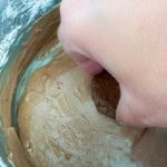 A hand dips a Texas Sheet Cake Cookie into a bowl of rich chocolate batter.