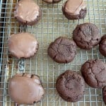 A cooling rack holds Texas Sheet Cake Cookies, some topped with a smooth chocolate glaze and some without, all placed on a baking sheet.