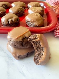 Texas Sheet Cake Cookies with glossy chocolate icing are stacked in front of a red tray, with one cookie showing a tempting bite taken out.