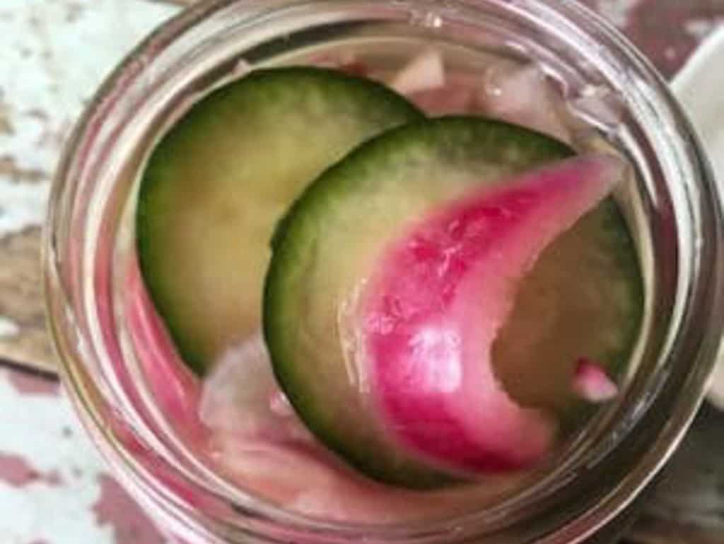 A glass jar containing slices of cucumbers and onions in a quick pickling solution, viewed from above.