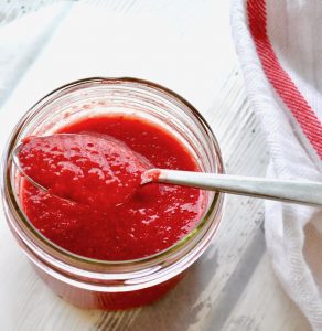 A jar of fresh strawberry puree with a spoon scooping.