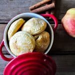 Mini apple hand pies on a small dish with fresh apples and cinnamon bark on the side.