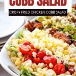 Enjoy a hearty Cobb Salad for dinner—a platter of chopped lettuce, cherry tomatoes, sweet corn, crispy fried chicken, bacon, and avocado, beautifully arranged on a white dish. Try this classic Cobb Salad Recipe tonight!.