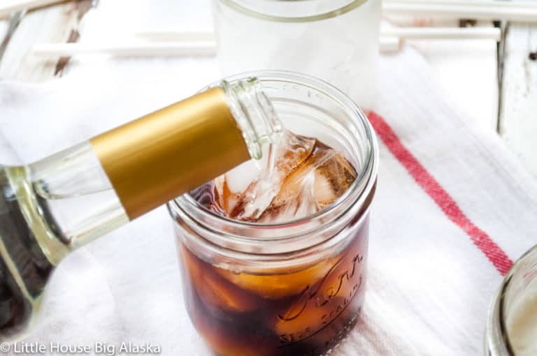 A mason jar filled with sweet cream iced coffee and a straw.
