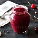A jar of cherry sauce beside fresh cherries.