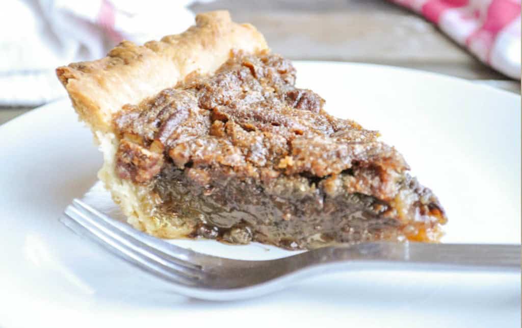 A slice of chocolate pecan pie on a white plate with a fork.