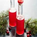 Two bottles of homemade cranberry vinegar with fresh cranberries on the side.