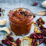 A jar full of vibrant red harissa with a spoon in it.
