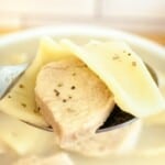 A spoon is holding a bowl of soup with meat in it.