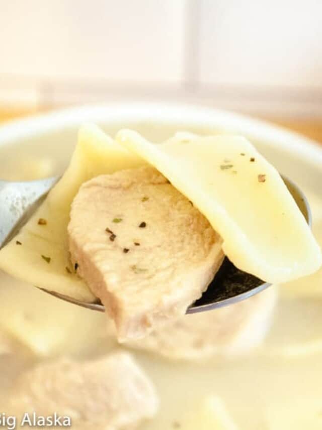 A spoon is holding a bowl of soup with meat in it.