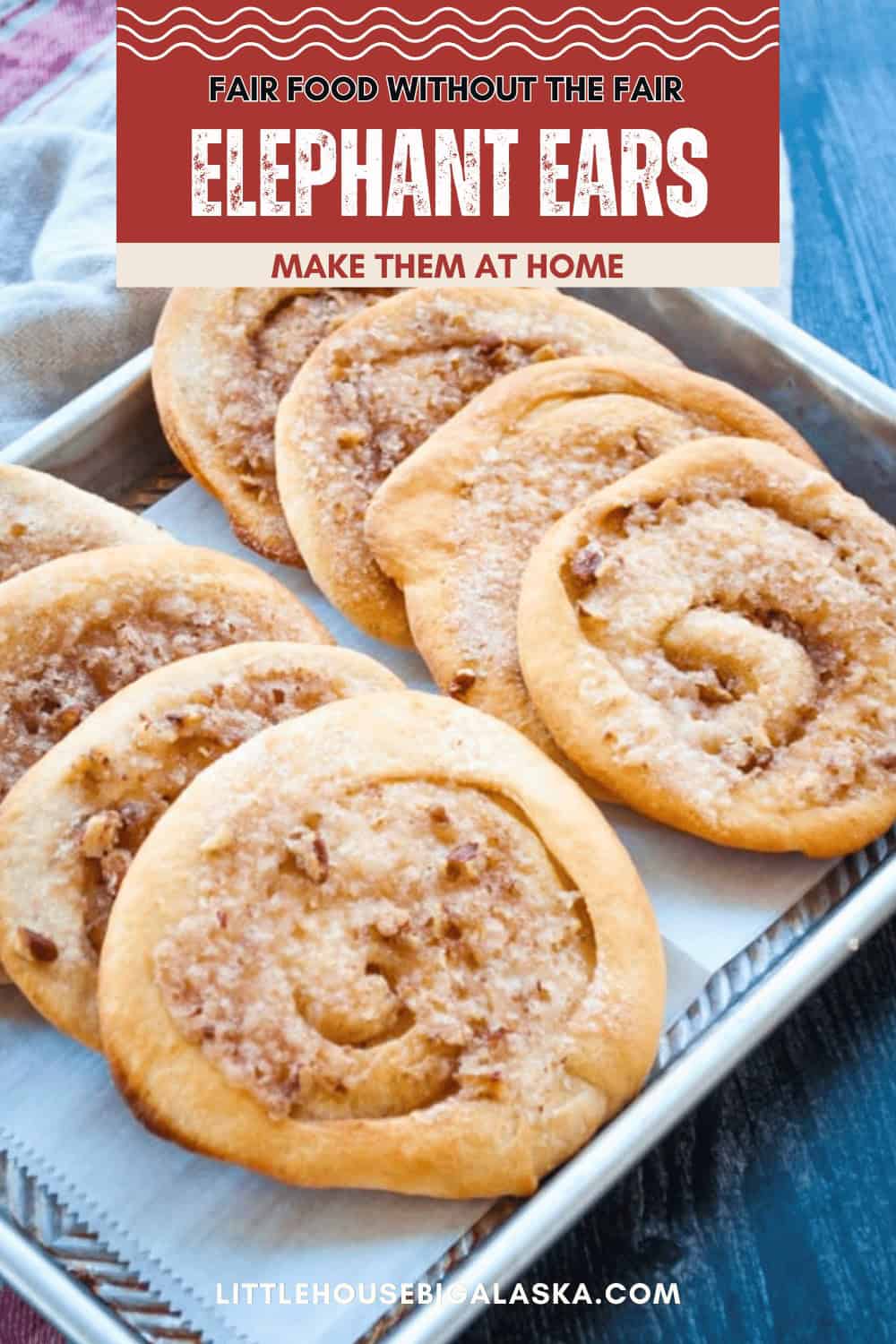 A tray of homemade elephant ear pastries topped with cinnamon sugar and nuts, with a sign above reading "Fair Food Without The Fair ELEPHANT EARS—Try This Easy Elephant Ears Recipe to Make Them At Home.