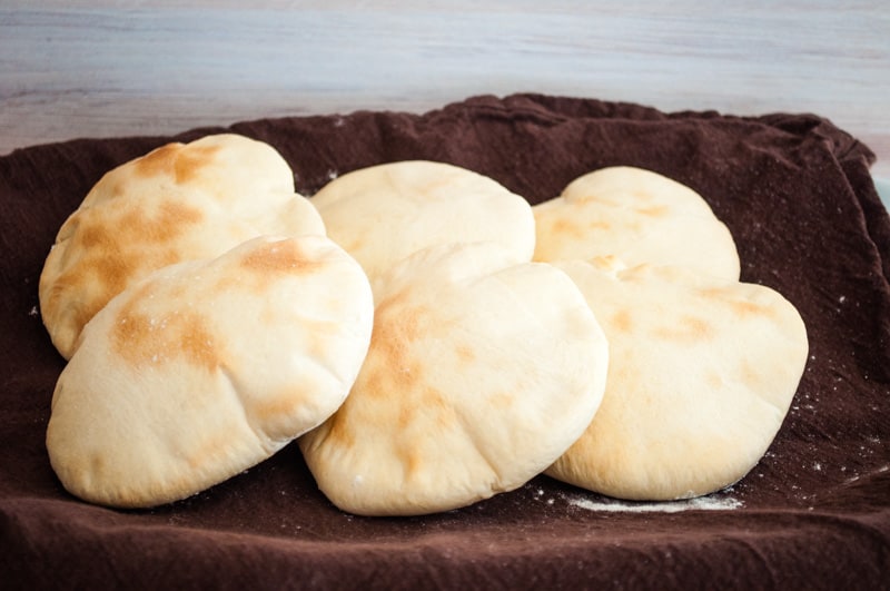 Freshly baked pita bread kept warm in a dishcloth on a platter.