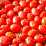 Seasoned grape tomatoes in a parchment lined baking pan ready to be roasted.