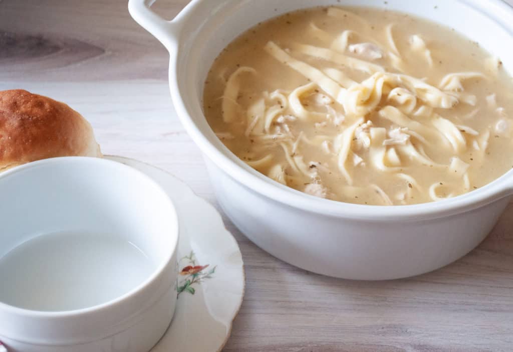 A pot of instant pot chicken and noodles soup with a bread on the side.