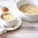 A pot and bowl of instant pot chicken and noodles soup with a bread on the side.
