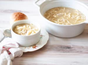 A pot and bowl of instant pot chicken and noodles soup with a bread on the side.