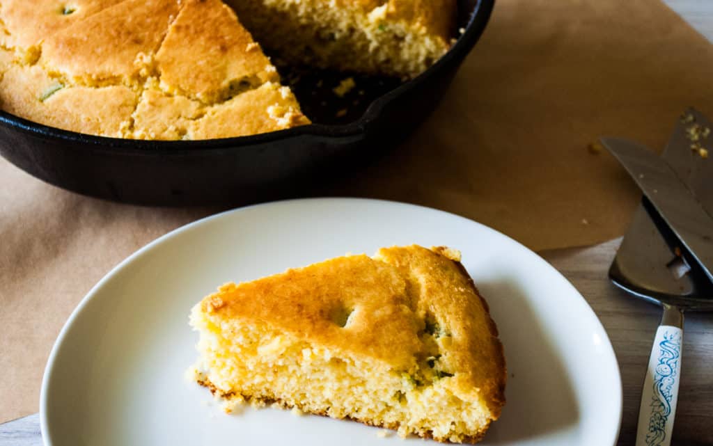 A slice of Jalape&ntilde;o cornbread with the rest of it in the background.