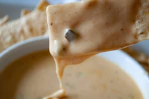 A chip dipping in melted queso cheese sauce you make at home.
