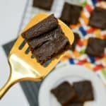 A slice if pumpkin brownie in a golden spatula with the rest of it in the background.