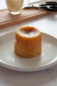 A freshly-steamed pudding served on a white plate.