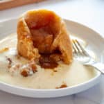 A sliced Sussex Pond Pudding, revealing a melted pond of butter, sugar, and a lemon wedge with cream anglaise around it.