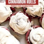A tray of Red Velvet Cinnamon Rolls topped with cream cheese icing, partially covered by a promotional banner describing them as perfect for celebrations.