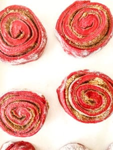 Four red velvet cinnamon rolls with sugar dusting arranged on a light background.
