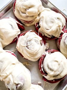 Freshly frosted red velvet cinnamon rolls on a tray.