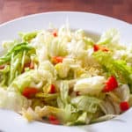 A fresh Buffalo Chicken Garden Salad with chopped lettuce and red bell peppers on a white plate.