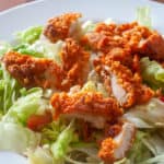 Crispy Buffalo Chicken Salad with lettuce and dressing on a white plate.
