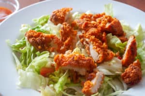 Crispy Buffalo Chicken Salad with lettuce and dressing on a white plate.