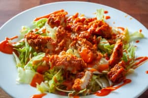 A plate of crispy Buffalo chicken salad drizzled with hot sauce.