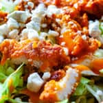 Close-up of a Buffalo Chicken Salad with lettuce, carrots, breaded chicken, cheese, and dressing.