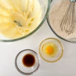 Ingredients laid out for baking Cream Cheese Sugar Cookies, including flour, eggs, vanilla extract, and softened butter.
