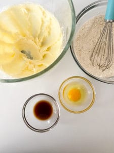 Ingredients laid out for baking Cream Cheese Sugar Cookies, including flour, eggs, vanilla extract, and softened butter.