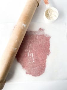 Red Velvet Sugar Cookie dough being rolled by a rolling pin.