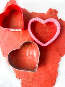 Three heart-shaped cookie cutters on Red Velvet Sugar Cookies dough.
