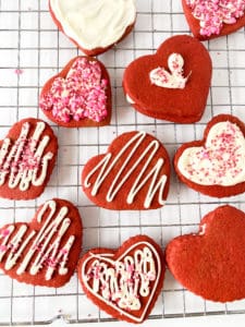 Red Velvet cut-out cookies with various icing and sprinkle decorations on a wire cooling rack.