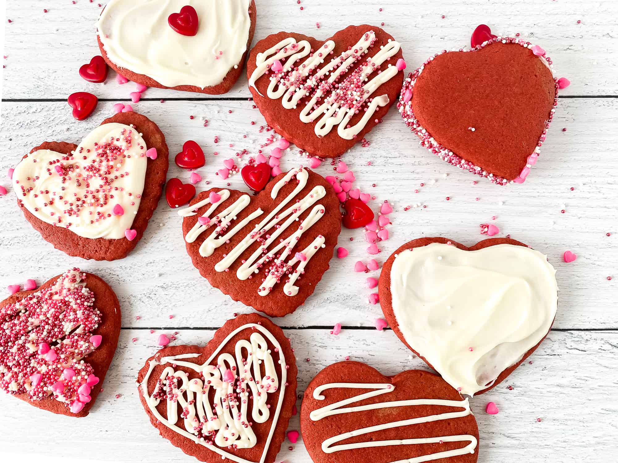 Red velvet sugar cookies with cream cheese frosting decorated with sprinkles.