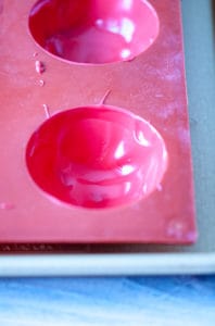 Red chocolate poured into a silicone mold to create a shell for a hot chocolate bomb.