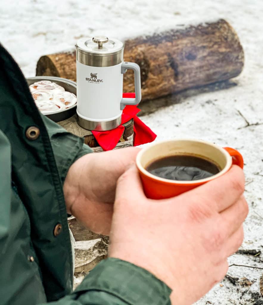 A person enjoys coffee and cinnamon rolls beside a Stanley Classic Stay Hot French Press.