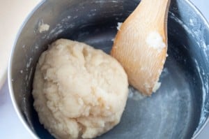 Pan with wooden spoon and churros dough in a ball.