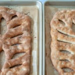 Two trays of freshly baked, lattice-top fougasse bread drizzled with kosher salt.
